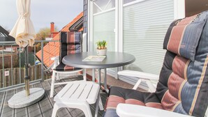 A balcony with a round table, two white chairs, and a cushioned sofa. - Exclusive vacation apartment in Norddeich, just a few minutes' walk from the sea. (Norden)