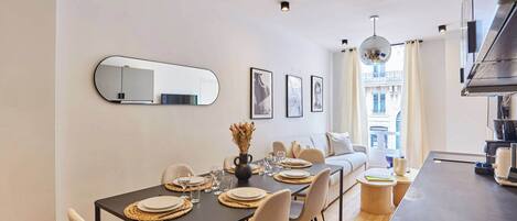 A modern dining area with a table set for four, a sofa, and a kitchen area with a large window.