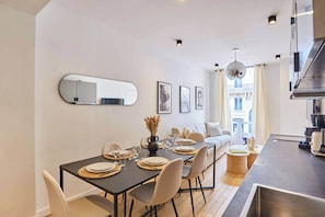 Uma zona de refeições moderna com uma mesa posta para quatro pessoas, um sofá e uma área de cozinha com uma janela grande.