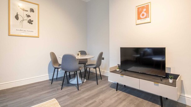 Ein modernes Wohnzimmer mit Fernseher, einem Esstisch mit vier Stühlen und zwei gerahmten Kunstwerken an den Wänden.