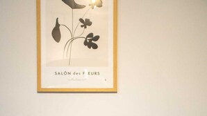 Ein Zimmer mit einem gerahmten Kunstwerk mit dem Titel 'SALON des FLEURS' an der Wand, einem grau gepolsterten Sessel und einem kleinen runden Tisch.