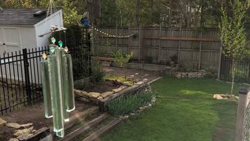A backyard with a wooden fence, a small shed, and a garden area with plants and a stone border.