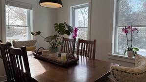 A dining area with a wooden table, chairs, a hanging light fixture, and potted plants. - Forest’s Edge Elora | Private Yard, Fire Pit, Near Downtown (Salem)