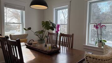A dining area with a wooden table, chairs, a hanging light fixture, and potted plants.