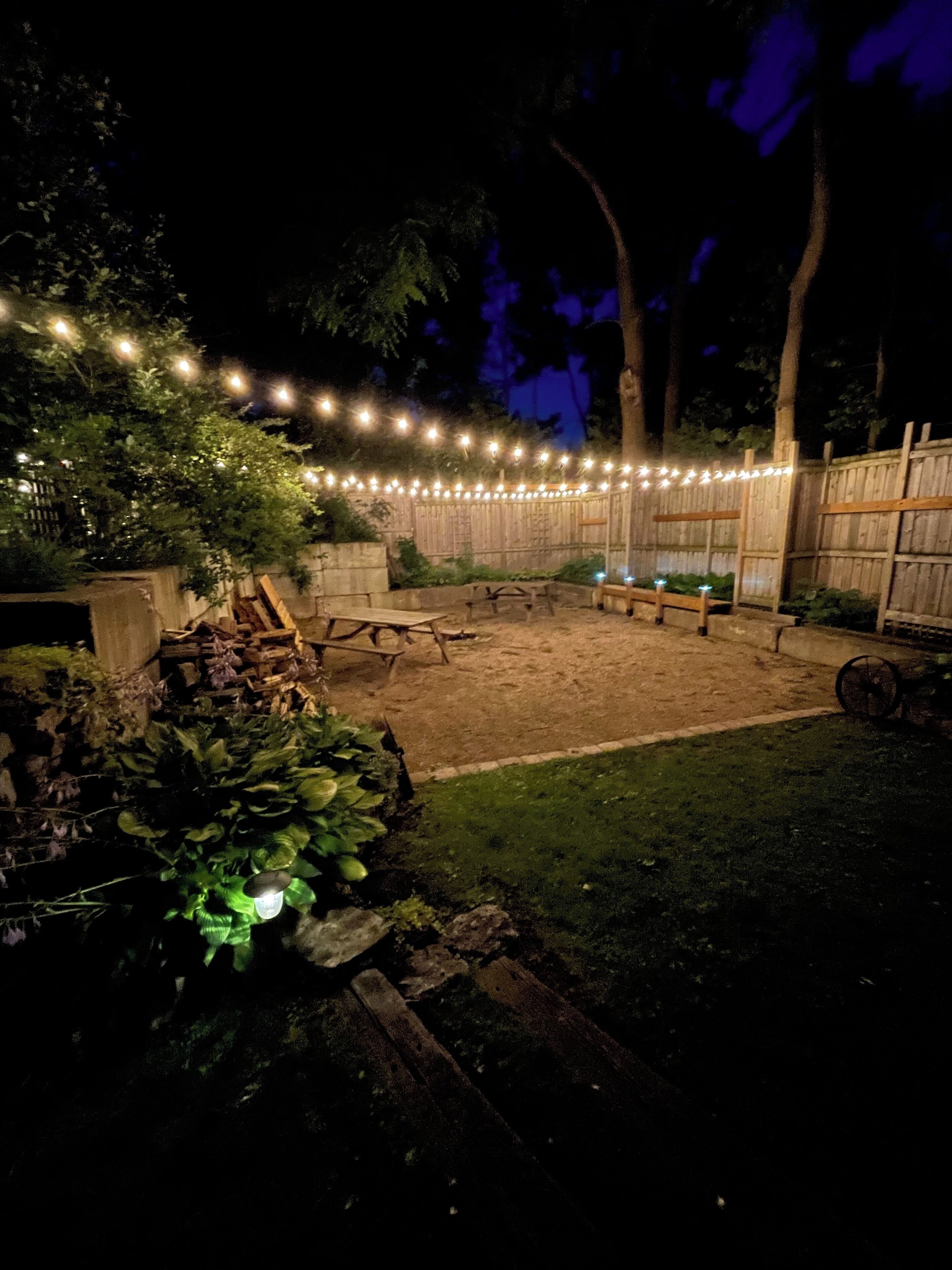 A backyard with a wooden deck, string lights, and a fire pit area.