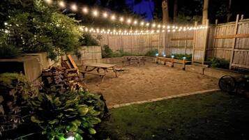 A backyard with a wooden deck, string lights, and a fire pit area.