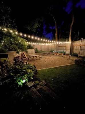 A backyard with a wooden deck, string lights, and a fire pit area.