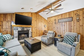 A cozy living room with a stone fireplace, a flat-screen TV, and a ceiling fan. - Lewiston Landing: Cozy Lake Access Getaway 3 Bedroom Home (Lewiston)