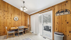 Una habitación con paneles de madera, una mesa de comedor, sillas, un candelabro, una puerta corredera de vidrio y un reloj de pared.