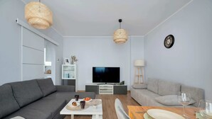Una sala de estar moderna con un sofá gris, una mesa de centro, un televisor y un comedor con una mesa preparada para dos.