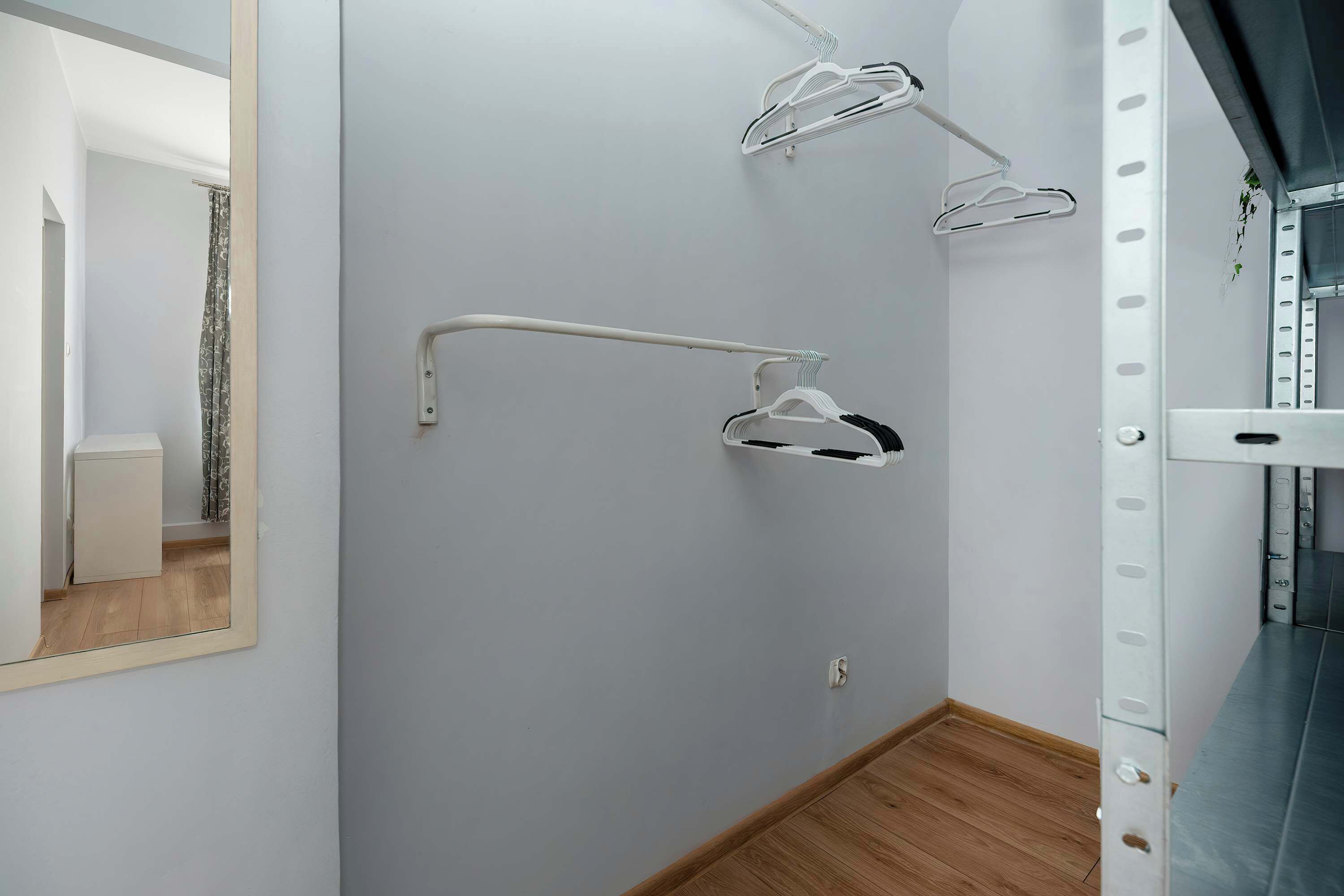 A room with a white wardrobe, a mirror, and a white wall-mounted rack with hangers.
