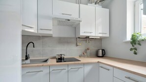 Una cocina moderna con armarios blancos, un grifo negro, un fregadero, un hervidor y una ventana con una planta.