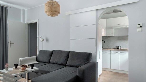 Una sala de estar moderna con un sofá seccional, una mesa de comedor con un mantel individual, y una cocina visible a través de un arco.