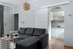A modern living room with a sectional sofa, a dining table with a placemat, and a kitchen visible through an archway. - Cozy Apartment in Torun | Desk to Work, Close to Park (Toruń)
