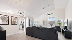 Un ampio soggiorno con un grande divano angolare grigio, una ventola a soffitto e opere d'arte alle pareti.