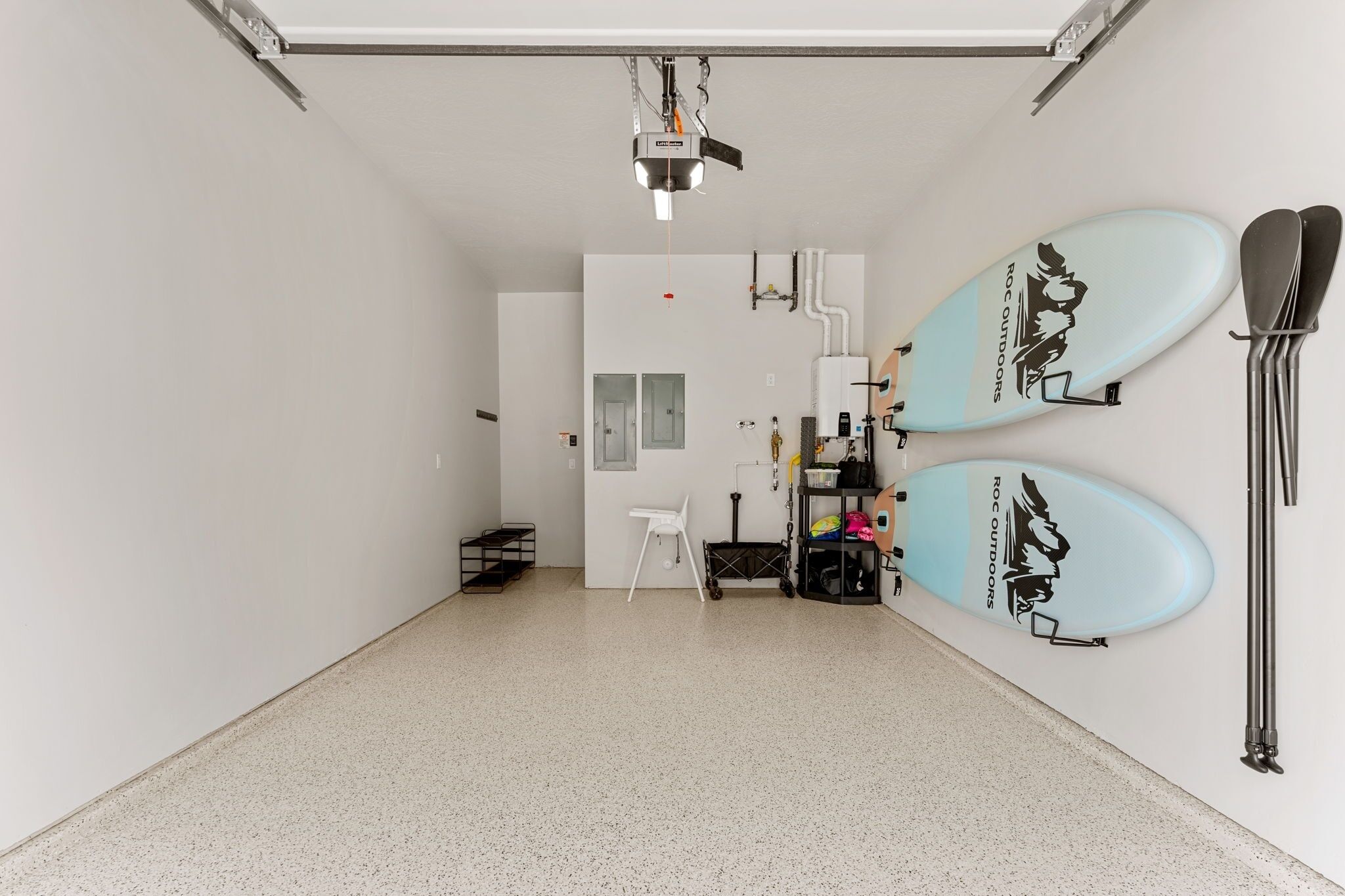 A room with a white interior, a ceiling-mounted projector, two surfboards on the wall, and a white chair.
