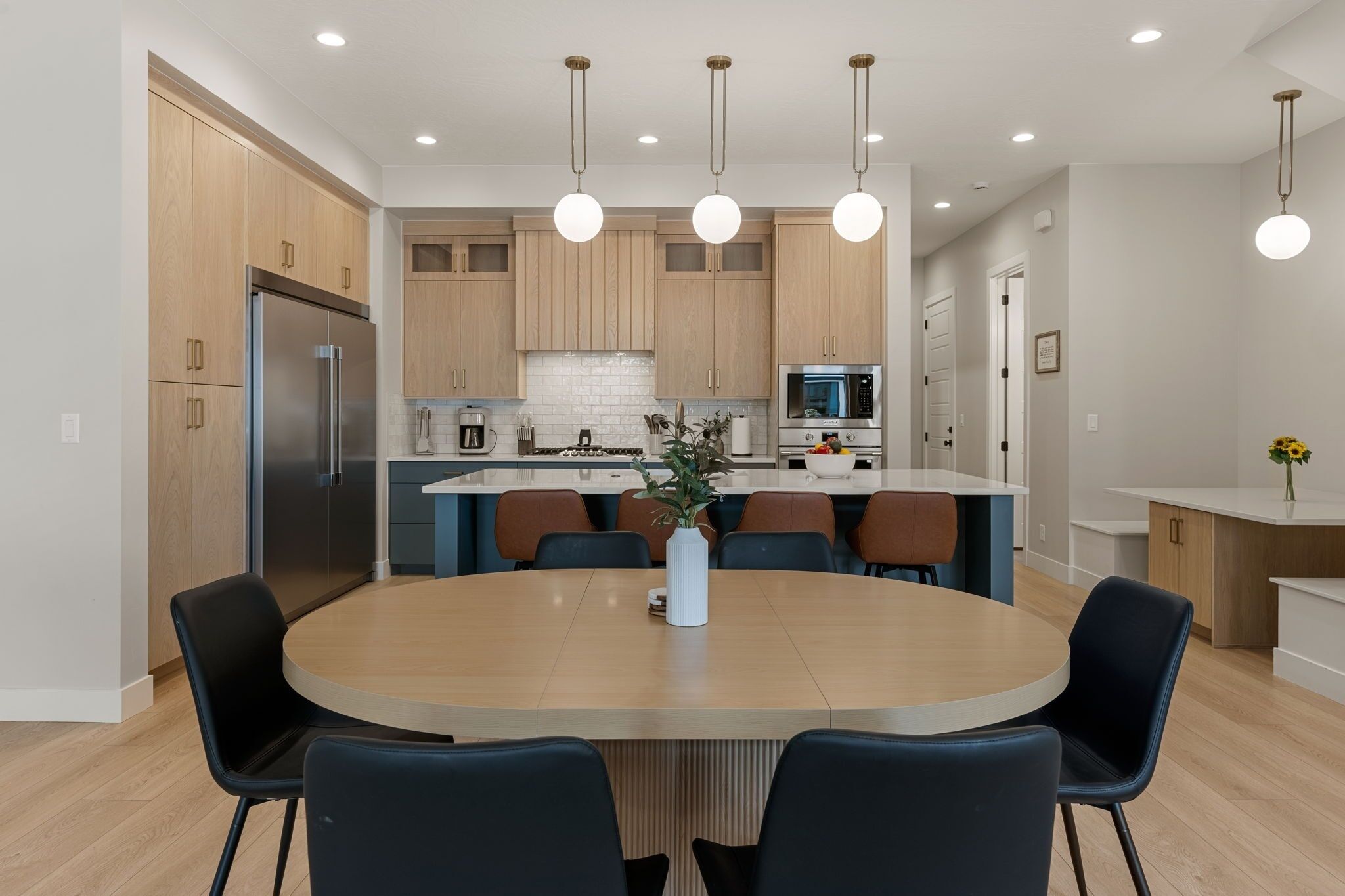 Une cuisine moderne avec des meubles en bois, un réfrigérateur en acier inoxydable, un four à micro-ondes et un coin repas comprenant une table ronde et des chaises.