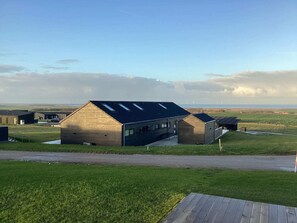 Ein modernes Gebäude mit geneigtem Dach und Oberlichtern, umgeben von grünen Feldern und blauem Himmel.