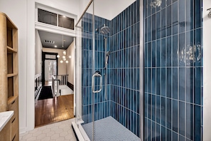 A modern bathroom with a glass-enclosed shower, blue-tiled walls, and a wooden floor. - Chic 2BR Near Forsyth Park w/ Courtyard, Parking by Lucky Savannah (Savannah)