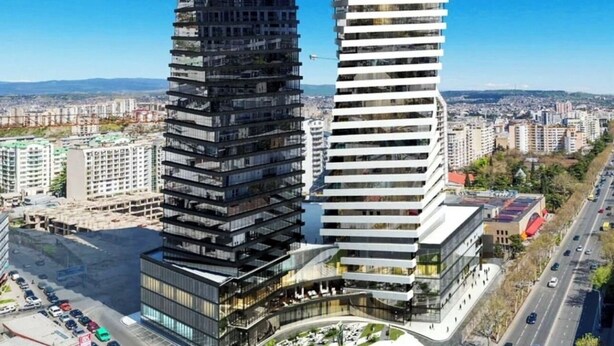 Dos edificios modernos de gran altura con un diseño curvo, rodeados por un paisaje urbano.