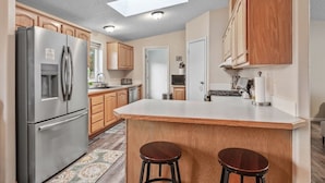 A kitchen with wooden cabinets, a stainless steel refrigerator, a central island with stools, and a skylight. - Atlas Farm Stay Retreat Patio/Hot Tub (Coeurdalene)