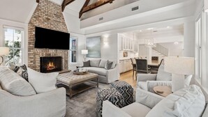 A spacious living room with a fireplace, comfortable seating, and a view of the kitchen and dining area. - Gorgeous 7 Bedroom 7 Bath Large Home with Carriage House in Gated WaterSound! (WaterSound)