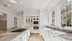 A modern kitchen with white cabinetry, a large island with a stovetop, a microwave, and a sink. - Gorgeous 7 Bedroom 7 Bath Large Home with Carriage House in Gated WaterSound! (WaterSound)