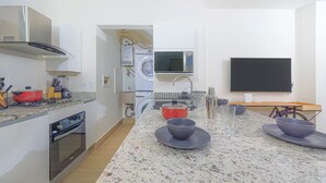 A modern kitchen with a built-in oven, microwave, and washing machine. There is a dining area with a table and chairs, and a large flat-screen TV mounted on the wall. - Reef Townhouse Tides -T39- (Punta Chame)