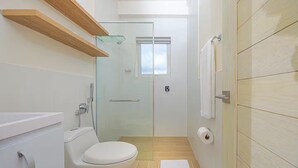 A modern bathroom with a toilet, shower, and glass door leading to a shower area. - Reef Townhouse Tides -T39- (Punta Chame)