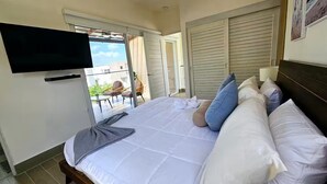 Ein Schlafzimmer mit einem Bett, Kissen, einem Fernseher und einem Balkon mit Stühlen.