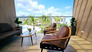 Ein Balkon mit Korbmöbeln, einem Glastisch und Blick auf einen Pool sowie Gebäude.