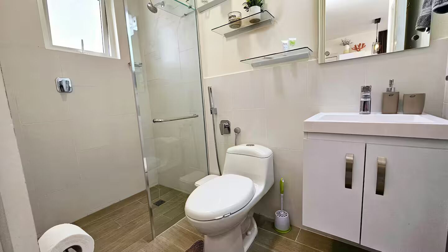 Une salle de bain moderne avec une douche à parois de verre, des toilettes blanches, un lavabo avec un miroir au-dessus et un meuble avec des tiroirs.