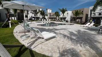 Um resort moderno com área de piscina, espreguiçadeiras e palmeiras.