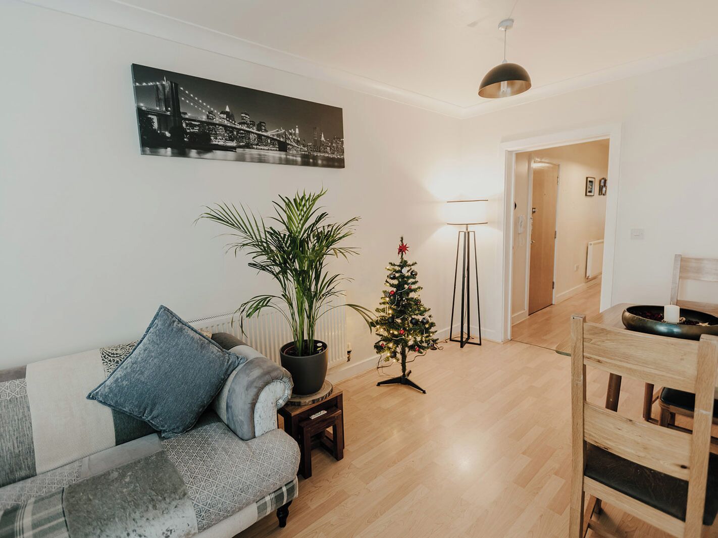 Ein Wohnzimmer mit einer Couch, einem kleinen Tisch mit Topfpflanze, einem Weihnachtsbaum und einer Stehlampe.