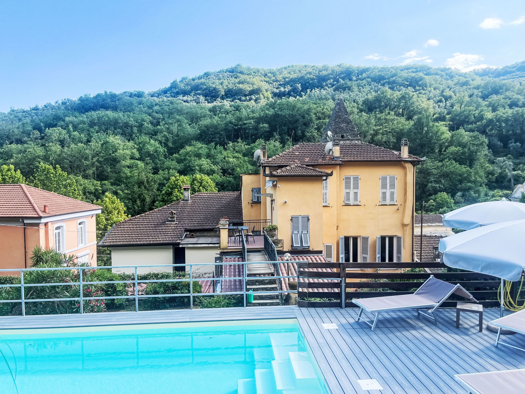 A pool area with lounge chairs, a wooden deck, and a building with a tiled roof.