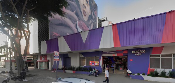 A building with a large mural, a 'Mercado extra' sign, and a 'No Parking' sign. - Estúdio charmoso com ótima localização (São Paulo)