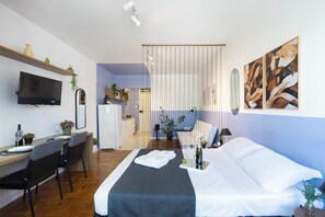 Una habitación de hotel con cama, escritorio con silla, televisión y zona de comedor con mesa y sillas.