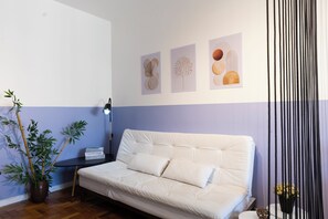 Una habitación moderna con un sofá blanco, una mesita con lámpara y una planta en maceta.