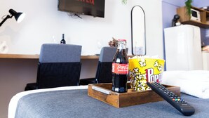 Ein gemütliches Wohnzimmer mit einem Fernseher, der 'NETFLIX' anzeigt, einer Coca-Cola-Flasche, einer Popcornschale und einer Fernbedienung auf einem Couchtisch.