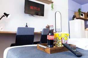 A cozy living room with a TV displaying 'NETFLIX', a bottle of Coca-Cola, a popcorn container, and a remote control on a coffee table. - Estúdio charmoso com ótima localização (São Paulo)