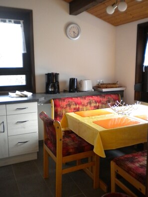 A small kitchen with a dining table, chairs, a clock, and a coffee maker. - Vacation Home in Hohenlupfen (67) - Meiß Öfingen (Bad Dürrheim)