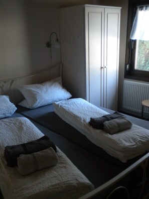 A bedroom with two single beds, a wardrobe, and a window with a view of greenery. - Vacation Home in Hohenlupfen (67) - Meiß Öfingen (Bad Dürrheim)