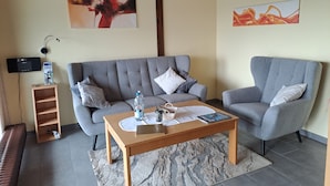 Ein modernes Wohnzimmer mit grauem Sofa, einem Holztisch und einem an der Wand montierten Fernseher.