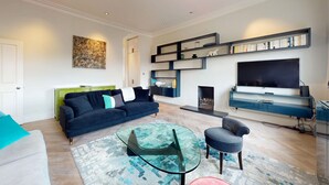 Un salon moderne avec un canapé, une table basse en verre, un téléviseur et une bibliothèque.