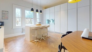 Une cuisine moderne dotée d’un îlot central, de luminaires suspendus et offrant une vue sur l’extérieur.