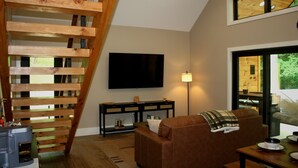 Een gezellige woonkamer met een houten trap, een flatscreen televisie, een bank en een eettafel.