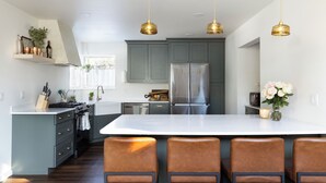 A modern kitchen with grey cabinets, a large island, and four brown bar stools. - Modern Chalet with Spa Bathoom (Seward)