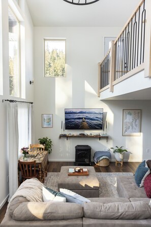 A spacious living room with a large flat-screen TV, a fireplace, a dining area with a wooden table and chairs, and a cozy seating area with a sofa and ottoman.