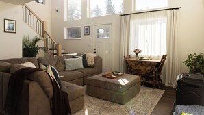 A living room with a sectional sofa, a wooden dining table, and a staircase. - Modern Chalet with Spa Bathoom (Seward)