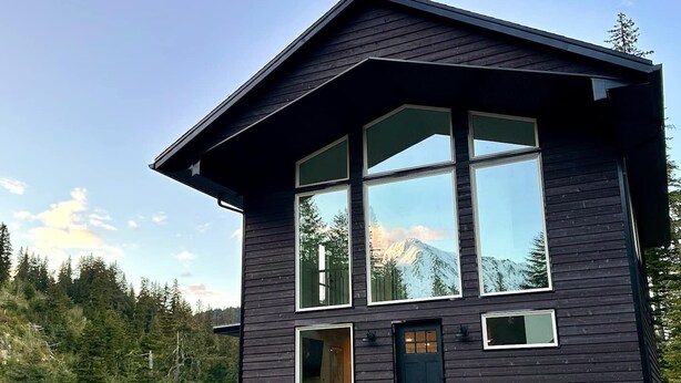 A modern two-story cabin with large windows, a deck, and a mountain view. - Modern Chalet with Spa Bathoom (Seward)